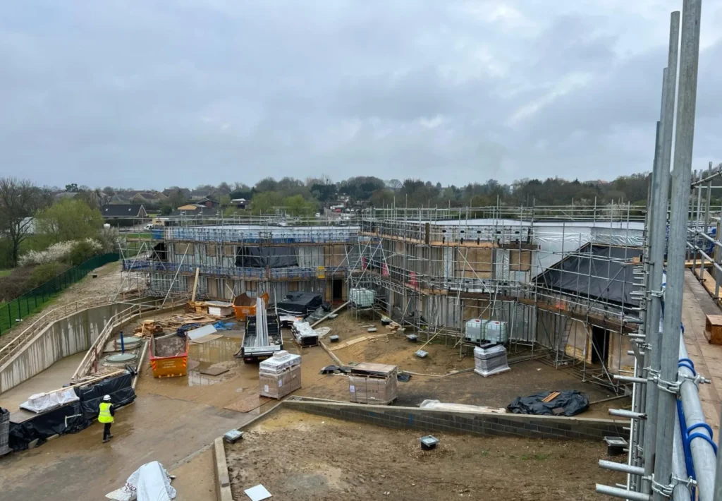 Large residential construction site in Waltham Abbey with extensive perimeter scaffolding, access platforms, and temporary edge protection installed by AB Scaffolding London.